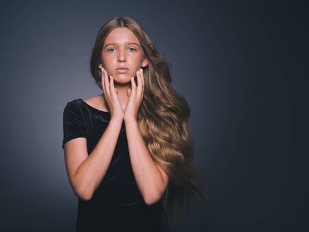 Long hair beauty girl healthy curly long hairstyle blonde in black dress. Studio shot.の写真素材