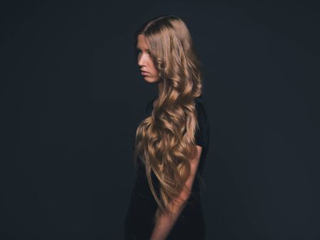Long hair beauty girl healthy curly long hairstyle blonde in black dress. Studio shot.の写真素材