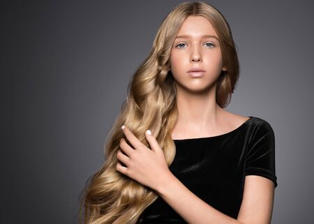Long hair beauty girl healthy curly long hairstyle blonde in black dress. Studio shot.の写真素材