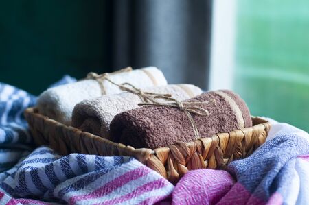 Decorative tiny towels in small wicker basket infront of window. Large towel on blurred background. Home decoration concept.の写真素材