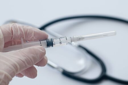 Scientist woman holding a vaccine syringe on blurred background with stethoscope. Concept of medical research, scientific study, coronavirus vaccine.の写真素材