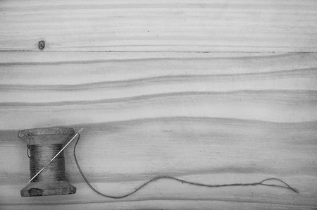 The old reel of thread and a needle on a wooden table in black and white.
