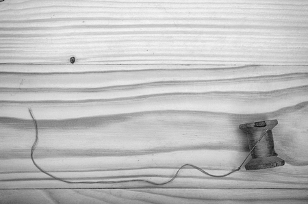 The old reel of thread and a needle on a wooden table in black and white.