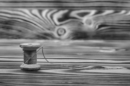The old reel of thread and a needle on a wooden table in black and white.の写真素材