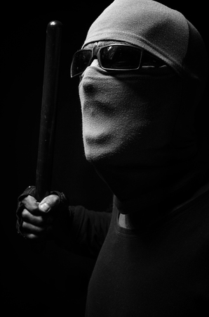 A man in a mask with a police baton in a black-and-white.の写真素材