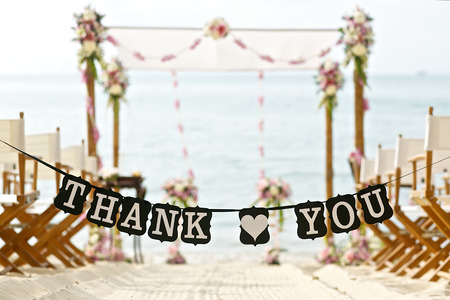 thank you words banner at beautiful beach wedding set up chairs flowers banana leaf cone