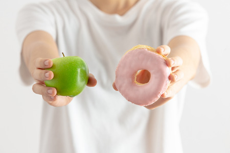 Female on dieting for good health concept. Young woman holding Donut and apple. Sweets Are Unhealthy Junk Food. Dieting, Healthy Eating, Lifestyle. Weight Loss. Obesity.の写真素材