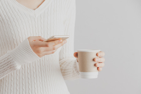Soft focus young girl hands using smartphone and hold a cup of coffee.の写真素材