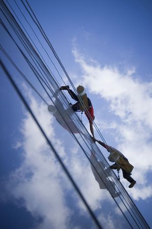 Two persons climbing building, connecting their hands