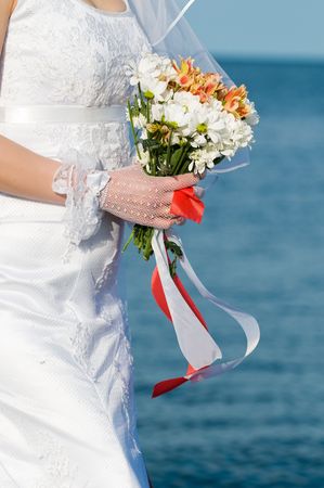 Close-up of bride with flowers over blue sea background の写真素材