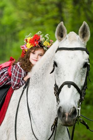 Beautiful little girl in floral wreath riding horse in the forest の写真素材