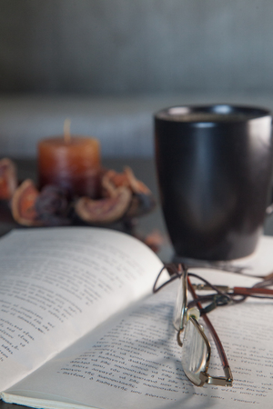 Vertical image of eyeglasses on top of open book with black mug in the backgroundの写真素材
