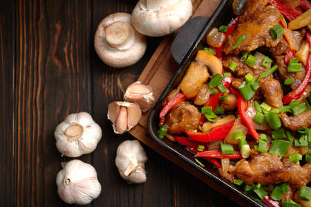 Fried meat with vegetables, green onions, bell peppers and mushrooms, in a frying pan, on a wooden backgroundの写真素材