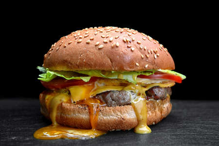 Burger, cheeseburger, hamburger with meat cutlet, cheese, lettuce and tomato, on a black backgroundの写真素材