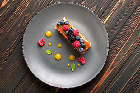 One piece of pie, honey cake with fresh berries, mint, and caramel, on a wooden backgroundの写真素材