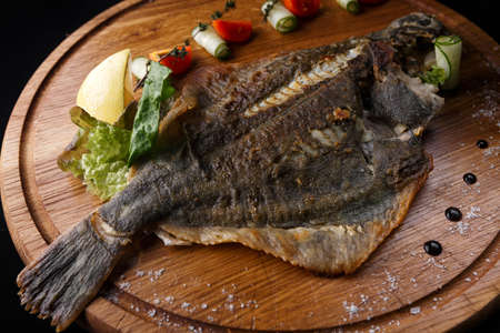 Fried fish flounder with lemon and vegetables on a wooden boardの写真素材