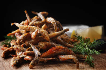 Fried anchovy fish on a wooden board with sauce and lemonの写真素材