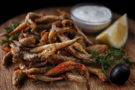Fried anchovy fish on a wooden board with sauce and lemonの写真素材