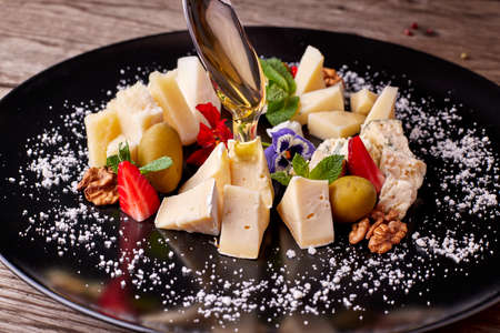 Cheese platter on a black plate with pouring honeyの写真素材