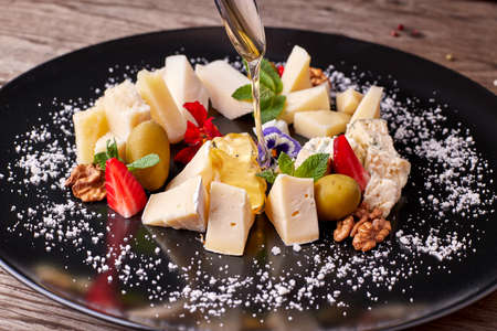 Cheese platter on a black plate with pouring honeyの写真素材