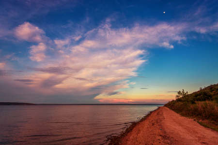 Beautiful sunset over the lake, with clouds and a road along the shore stretching into the distanceの写真素材