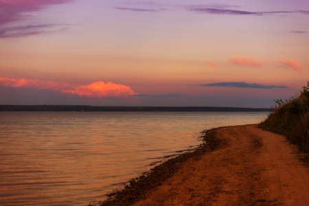 Beautiful sunset over the lake, with clouds and a road along the shore stretching into the distanceの写真素材