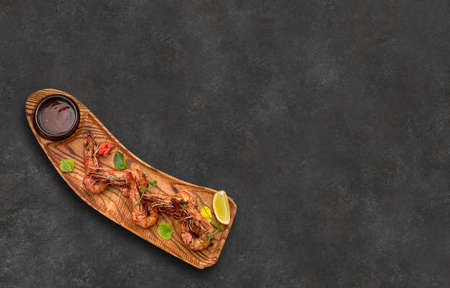 Grilled shrimp with lemon and sauce, on a wooden board, on a gray background, with place for text,...