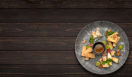 Cheese platter with grapes and honey, on a plate, on a wooden background. Horizontal photoの写真素材