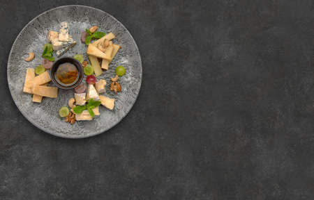 Cheese platter with grapes and honey, on a plate, on a gray concrete background. Horizontal photoの写真素材