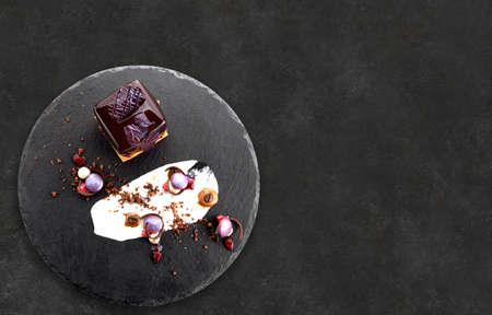 Dessert with nuts in chocolate glaze in the shape of a cube on black slateの写真素材