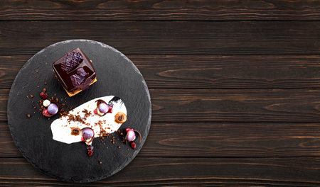 Dessert with nuts in chocolate glaze in the shape of a cube on black slateの写真素材