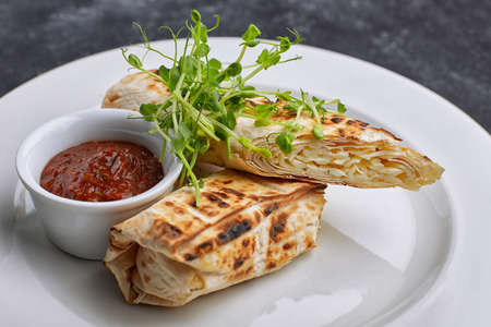 Pita bread with suluguni cheese, sauce, microgreen, on a white plate, on dark concrete. Cooked on the grillの写真素材