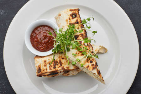 Pita bread with suluguni cheese, sauce, microgreen, on a white plate, on dark concrete. Cooked on...
