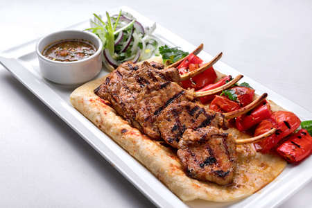 Pork, lamb ribs on pita bread, with baked bell pepper and sauce, on a white plate, on a white backgroundの写真素材