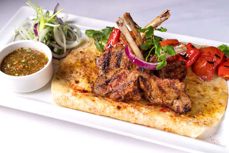 Pork, lamb ribs on pita bread, with baked bell pepper and sauce, on a white plate, on a white backgroundの写真素材