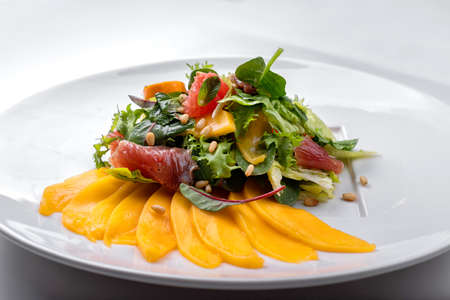 Mix mango salad, with jerky, grapefruit, pine nuts and mint, on a white plate, white backgroundの写真素材