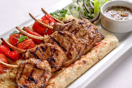 Pork, lamb ribs on pita bread, with baked bell pepper and sauce, on a white plate, on a white backgroundの写真素材