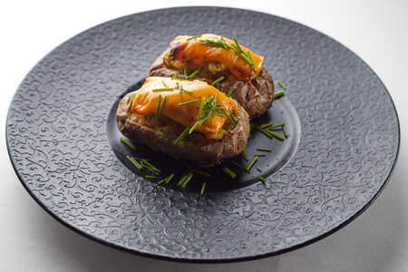 Baked potato with cheese and herbares, on a black plateの写真素材