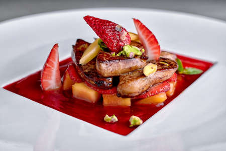 Foie gras in strawberry sauce with pear and strawberry pieces on white plateの写真素材