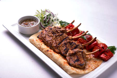 Pork, lamb ribs on pita bread, with baked bell pepper and sauce, on a white plate, on a white backgroundの写真素材