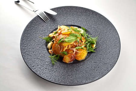 Fried potatoes with garlic and herbs on a black plate on a white backgroundの写真素材