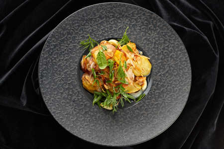 Fried potatoes with garlic and herbs on a black plate on a black backgroundの写真素材