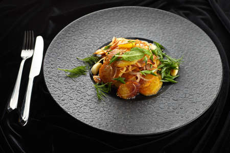 Fried potatoes with garlic and herbs on a black plate on a black backgroundの写真素材