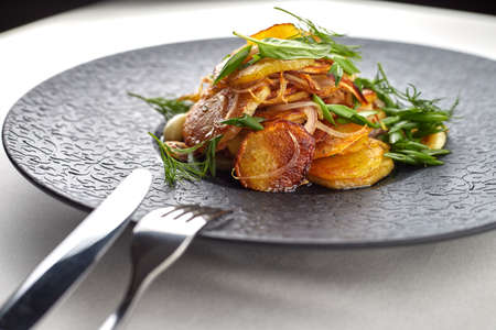 Fried potatoes with garlic and herbs on a black plate on a white backgroundの写真素材