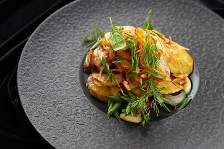 Fried potatoes with garlic and herbs on a black plate on a black backgroundの写真素材