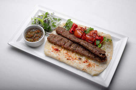 Lamb lula kebab, with baked tomatoes, onions and sauce, on a white plate, on a white backgroundの写真素材