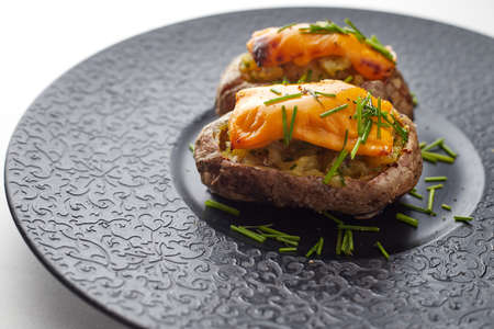 Baked potato with cheese and herbares, on a black plateの写真素材