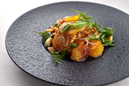 Fried potatoes with garlic and herbs on a black plate on a white backgroundの写真素材