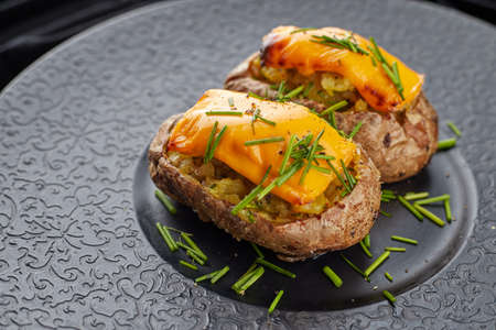 Baked potato with cheese and herbares, on a black plateの写真素材