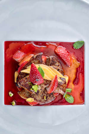 Foie gras in strawberry sauce with pear and strawberry pieces on white plateの写真素材